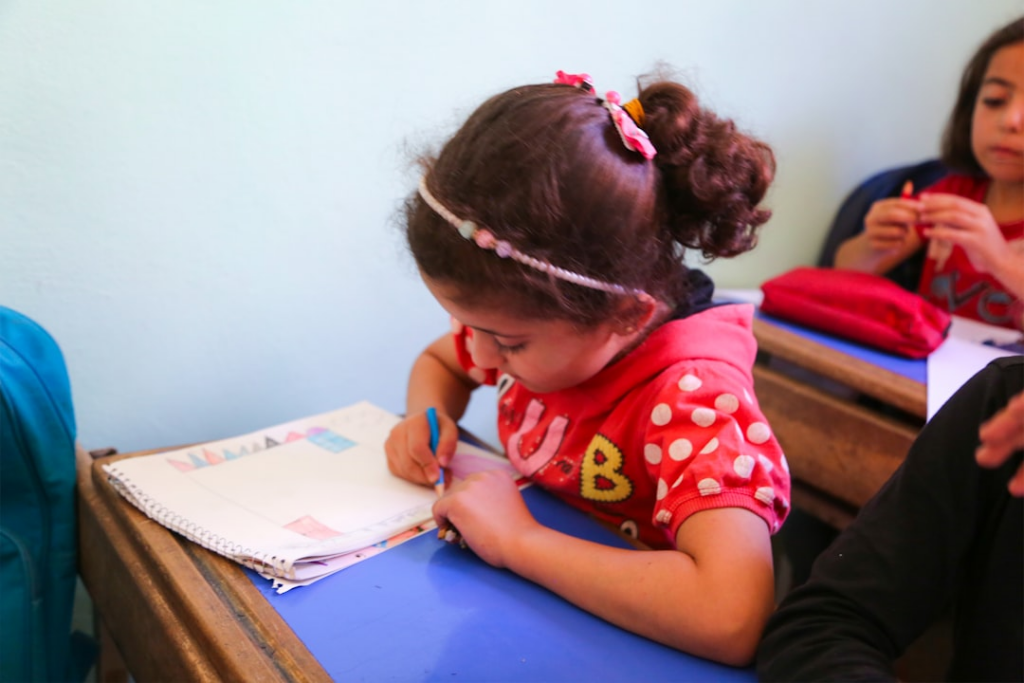 A little girl sitting at a desk writing on a piece of paper — Foto por ‪Salah Darwish na Unsplash