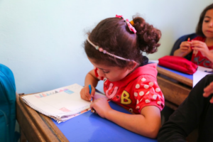 A little girl sitting at a desk writing on a piece of paper — Foto por ‪Salah Darwish na Unsplash