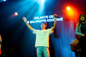 A man standing on a stage with his arms in the air — Foto por Alex Gallegos na Unsplash