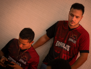 Two men in matching red and black jerseys leaning together. — Foto por Alef Morais na Unsplash