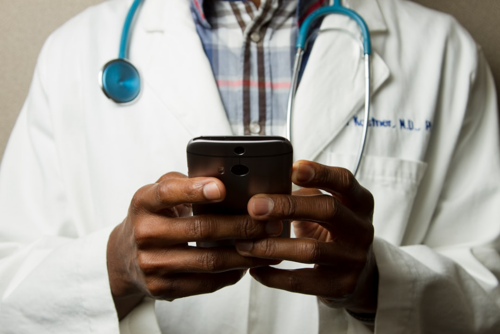 person wearing lavatory gown with green stethoscope on neck using phone while standing — Foto por National Cancer Institute na Unsplash